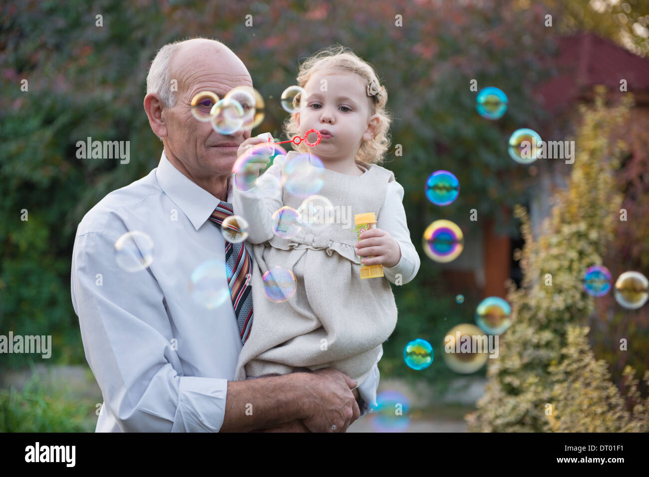 Heureux grand-père et petite-fille curly mignon soufflant des bulles de savon Banque D'Images