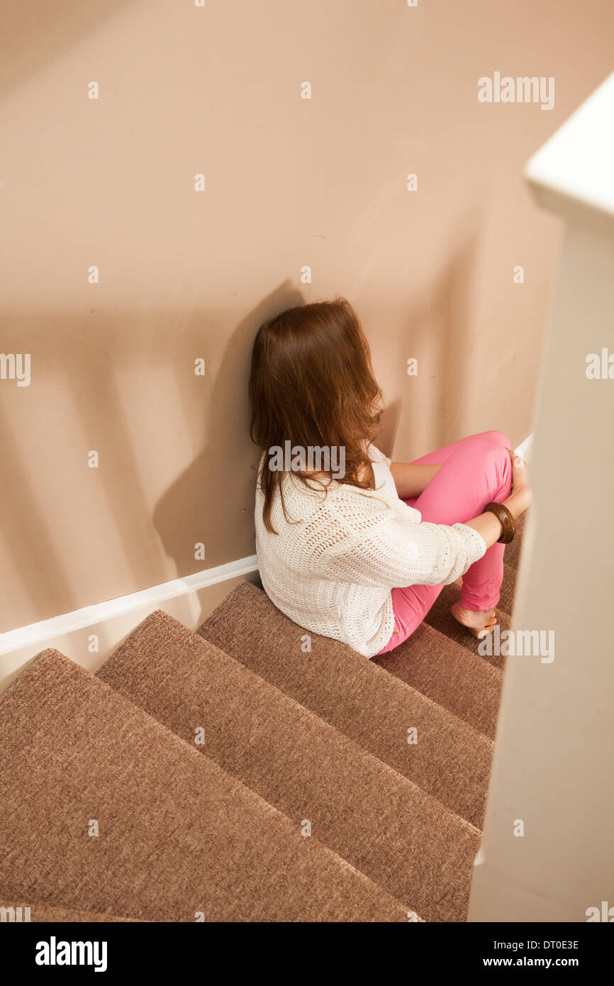 Plus d'épaule d'une jeune femme assise sur les escaliers à l'écart de l'appareil photo. Banque D'Images
