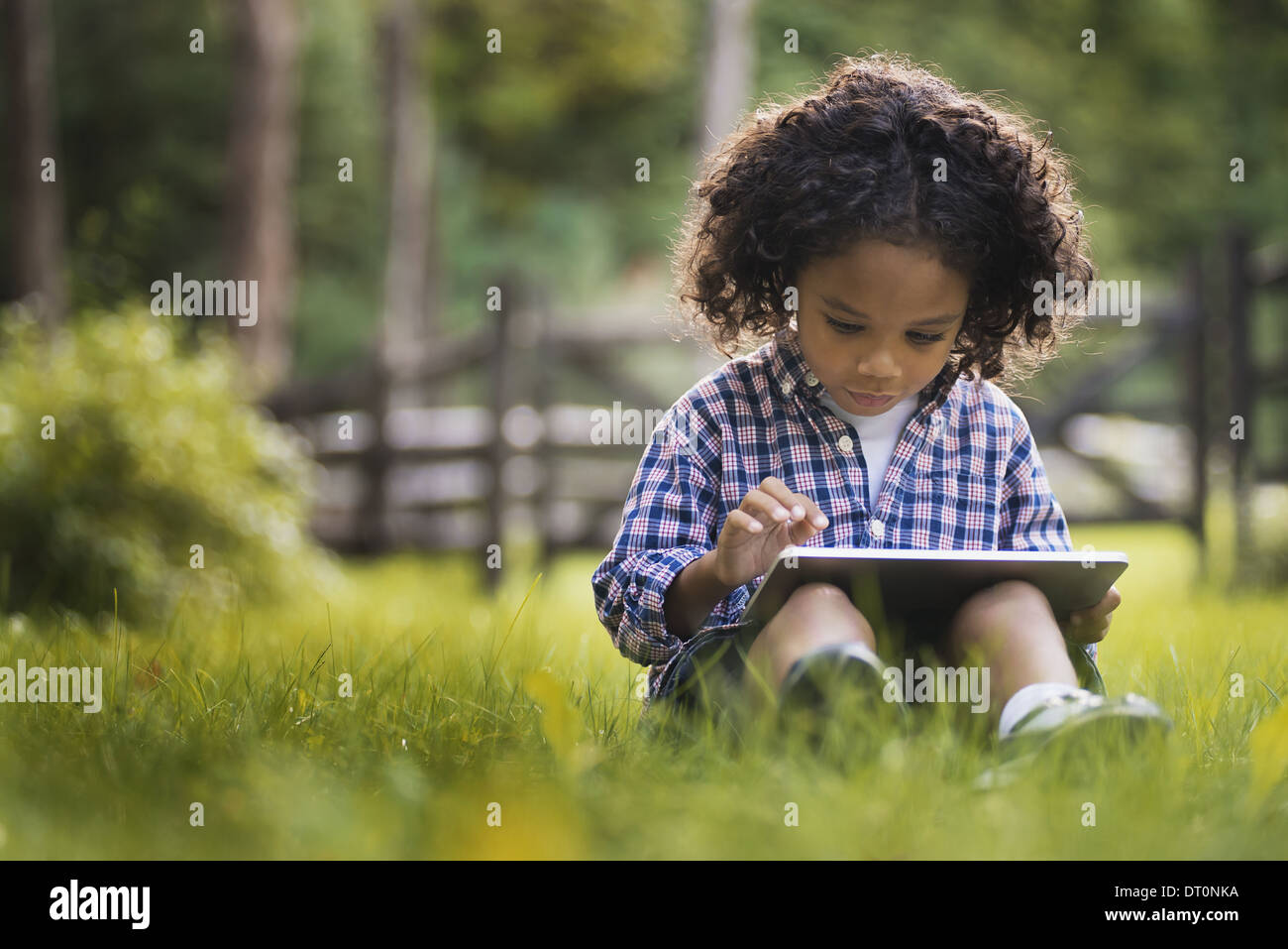 Woodstock, New York USA petit boy sitting on grass using digital tablet Banque D'Images