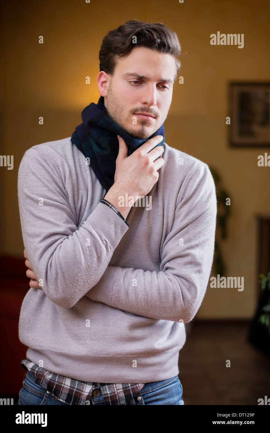 Jeune homme avec écharpe, tenant son cou à cause de maux de gorge, à la maison dans son salon Banque D'Images
