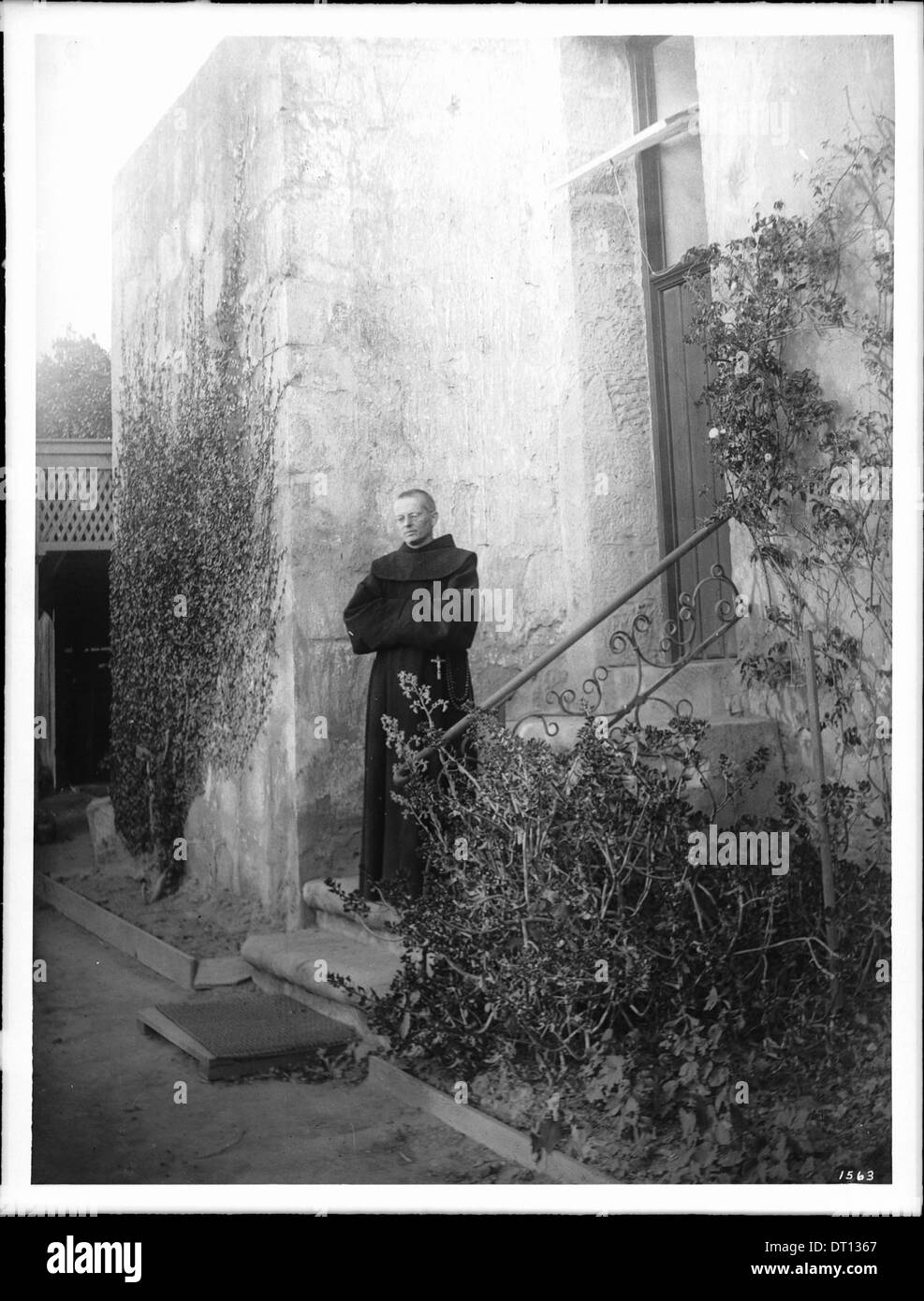 Un prêtre franciscain se tient sur une marche inférieure des escaliers extérieurs de la Mission Santa Barbara, capturé entre 1898 et 1900, reflétant le cadre historique de la mission. Banque D'Images