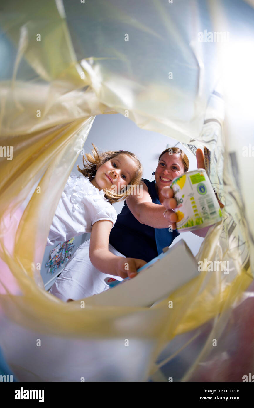 Le tri des déchets ménagers de la famille : petite fille et sa mère jetant une matière recyclable peut dans un sac poubelle jaune Banque D'Images
