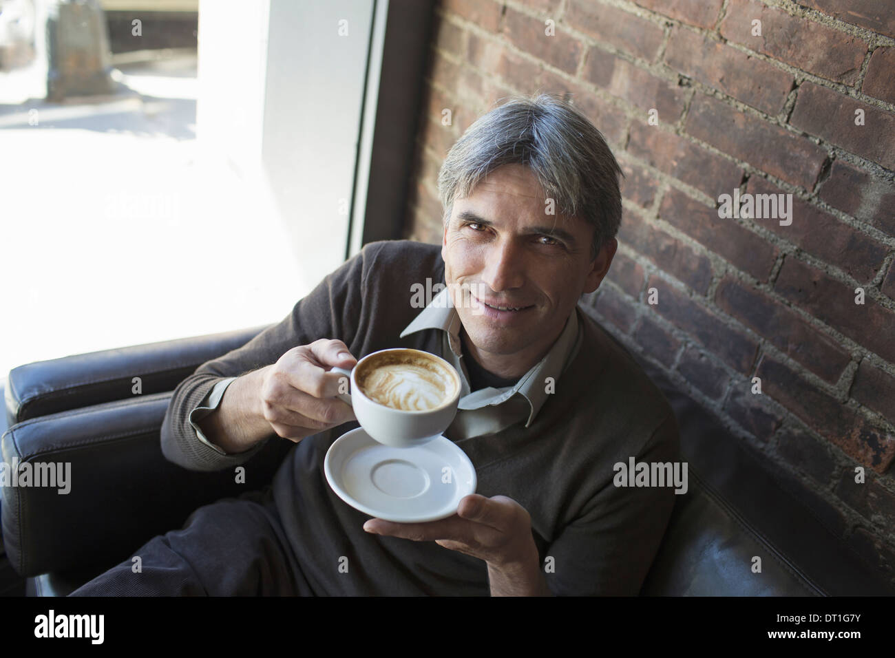 Un homme assis dans un café avec une tasse de cappuccino mousseux Banque D'Images