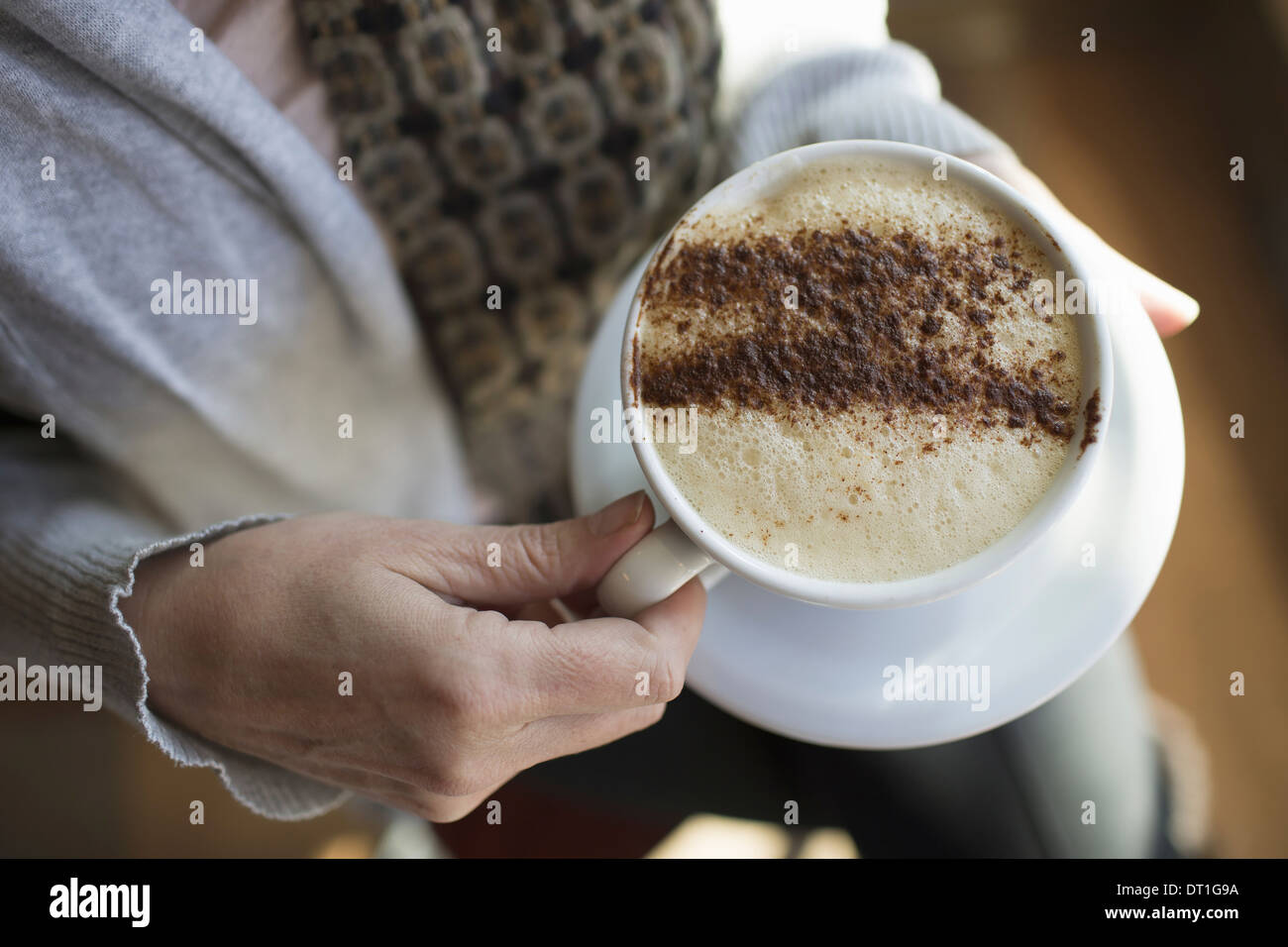 Une personne titulaire d'une pleine tasse de café cappuccino mousseux dans un livre blanc la chine tasse chocolat en poudre saupoudré dans un motif Banque D'Images