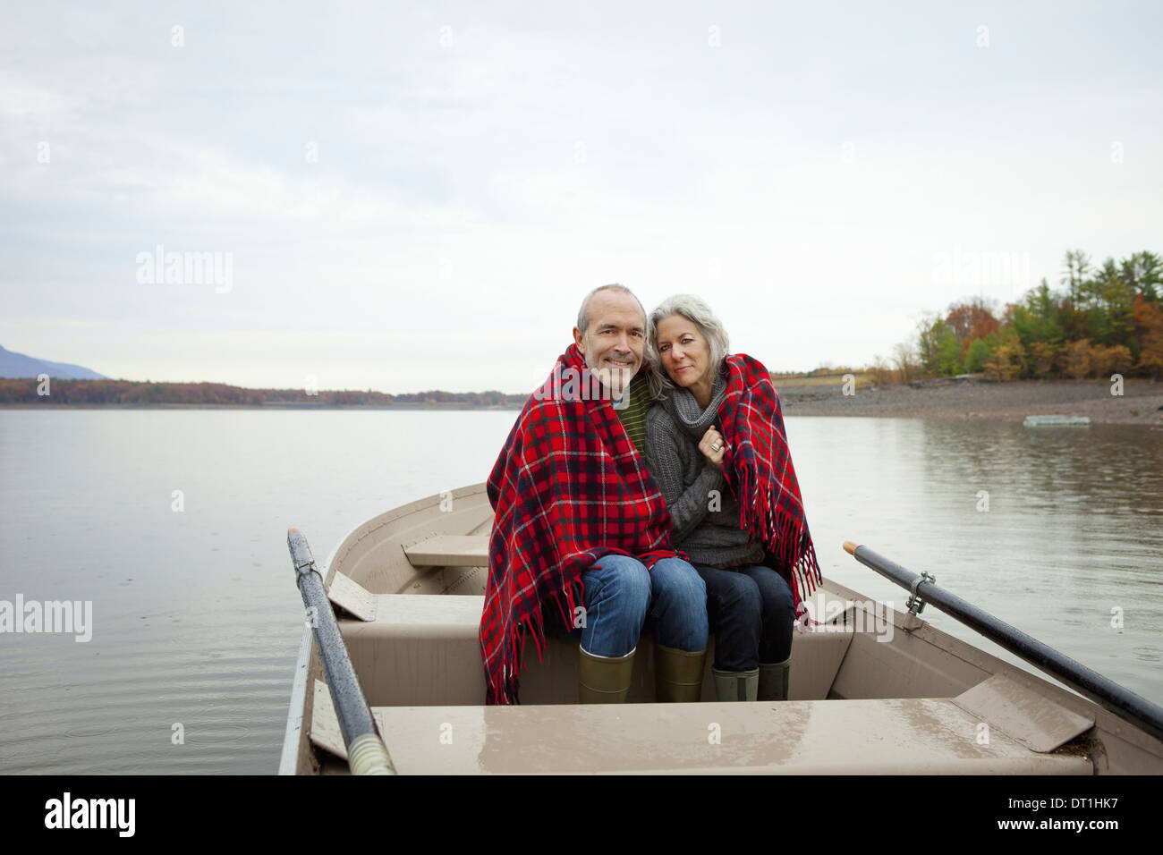 Un couple homme et femme assis dans un bateau à rames sur l'eau une journée d'automne, le partage d'un tapis de pique-nique pour garder au chaud Banque D'Images
