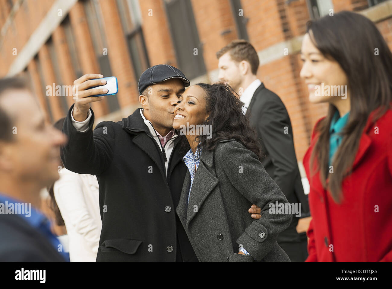 Un homme tenant un téléphone avec appareil photo et prendre des photos du groupe embrassant une jeune femme les hommes et les femmes Banque D'Images