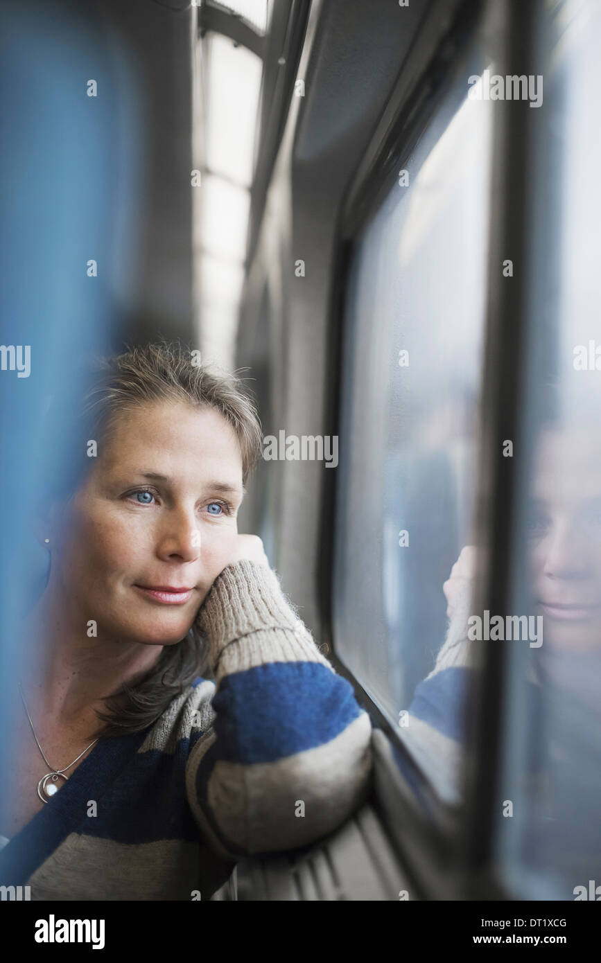 Une femme assise sur un siège côté fenêtre dans un train transport posant sa tête sur sa main à la recherche dans la distance Banque D'Images