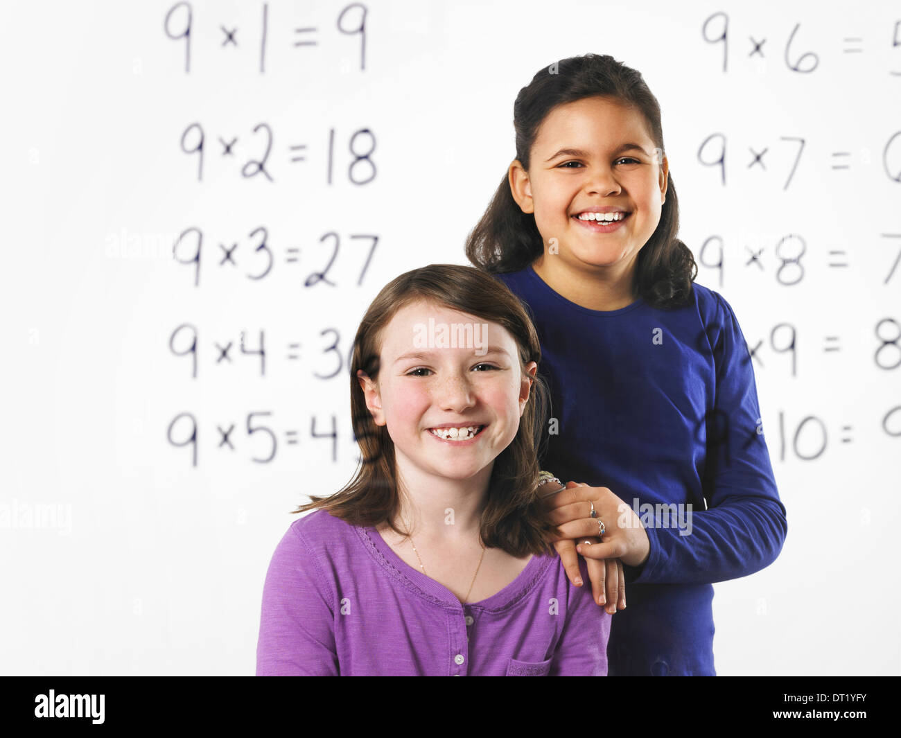 Deux jeunes filles à la recherche lors d'une série de tables de multiplication mathématique sur un mur clair voir au travers de l'apprentissage avec un stylo noir Banque D'Images