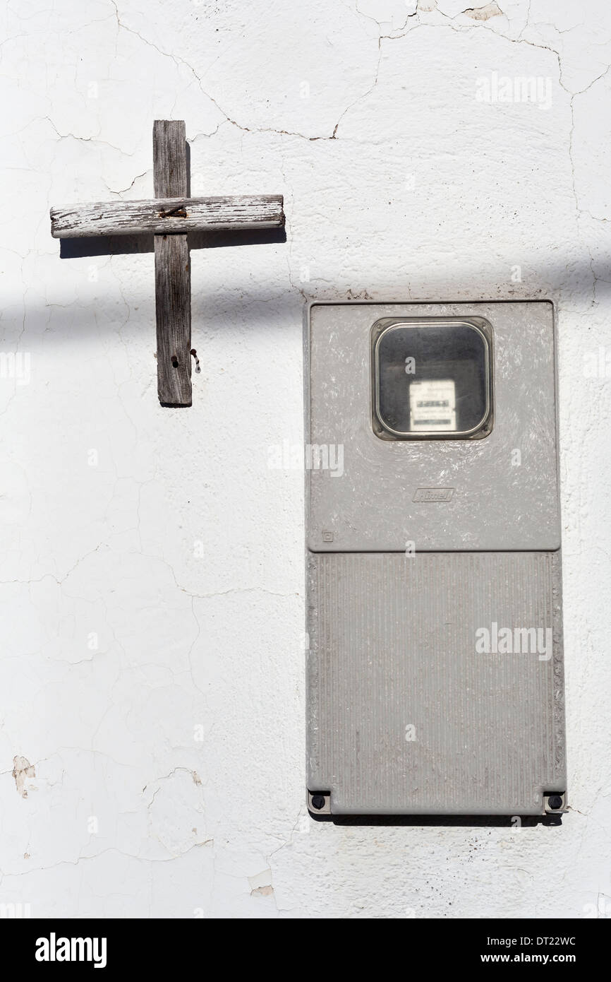 Compteur électrique et croix de bois sur le mur d'une maison. Banque D'Images