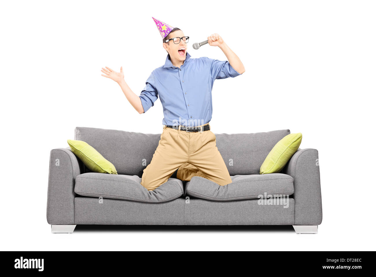 Jeune homme avec chapeau de fête en chantant dans le microphone assis sur un canapé Banque D'Images
