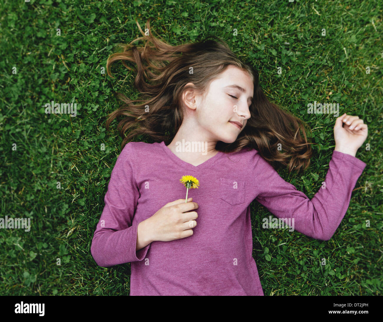 Une fillette de dix ans couché dans l'herbe avec ses yeux fermés tenant une fleur de pissenlit Banque D'Images
