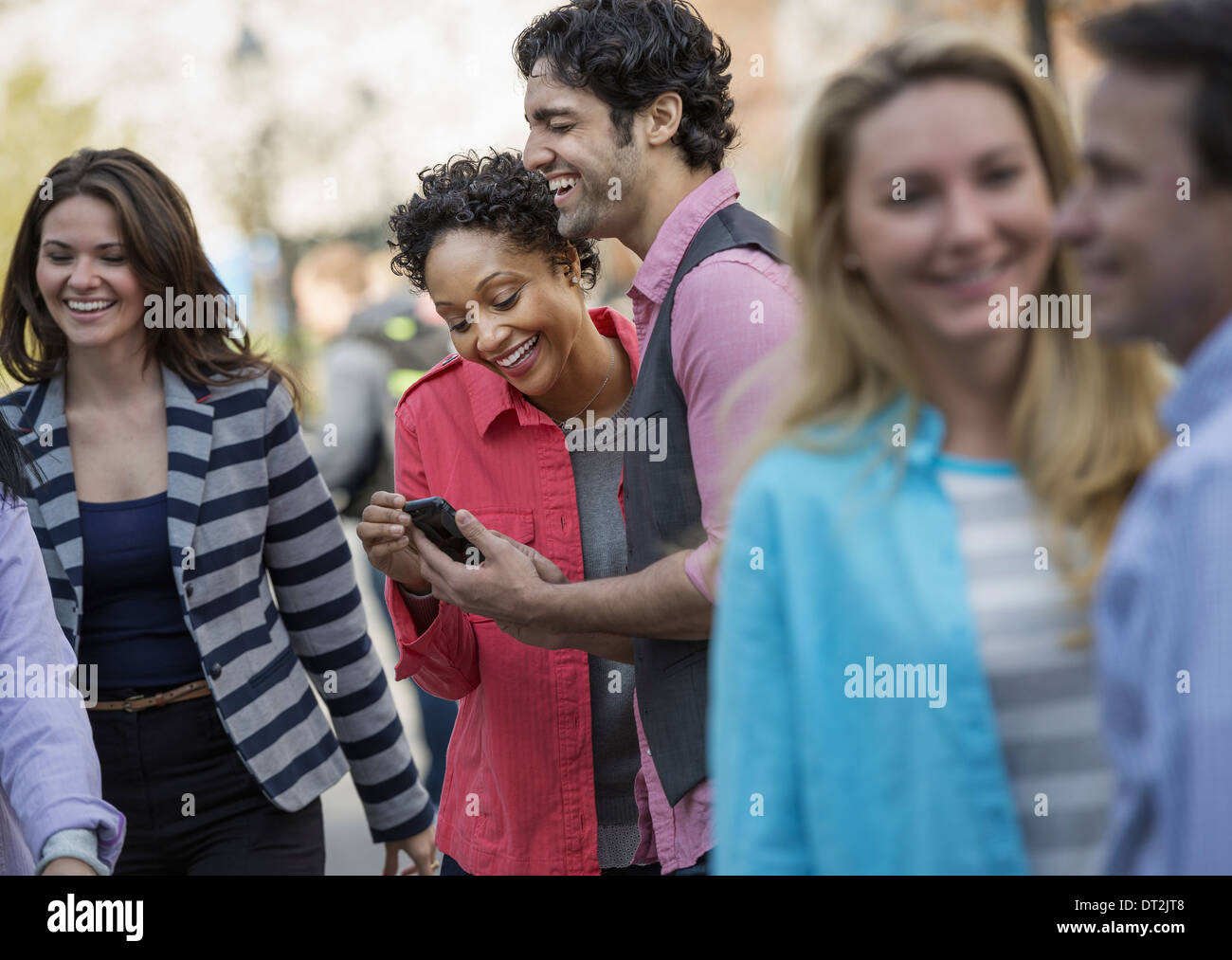 Les gens à l'extérieur dans la ville au printemps à deux à un écran de téléphone cellulaire et de rire Banque D'Images