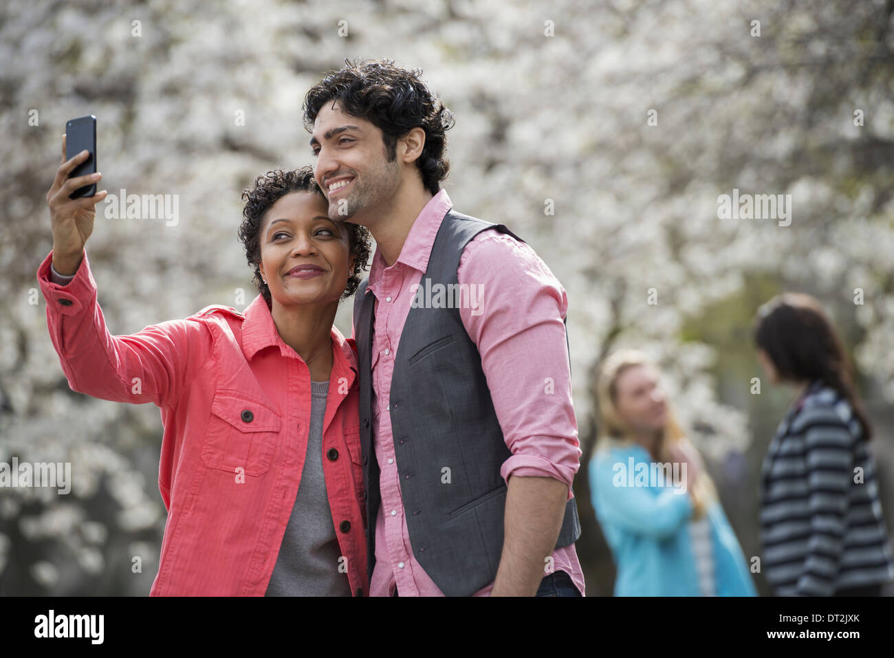 Temps de printemps fleurs blanches sur les arbres d'une jeune femme de prendre une photo d'elle-même et un jeune homme Banque D'Images Temps de printemps fleurs blanches sur les arbres d'une jeune femme de prendre une photo d'elle-même et un jeune homme Banque D'Images