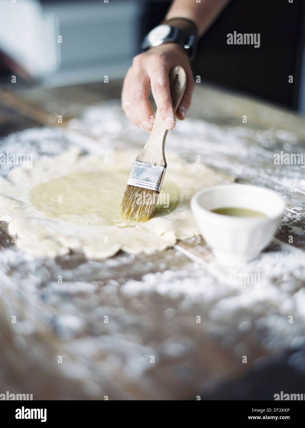 Une cuisine domestique d'une femme préparant un repas rouler une pâte sur une table et badigeonner avec l'oeuf Banque D'Images