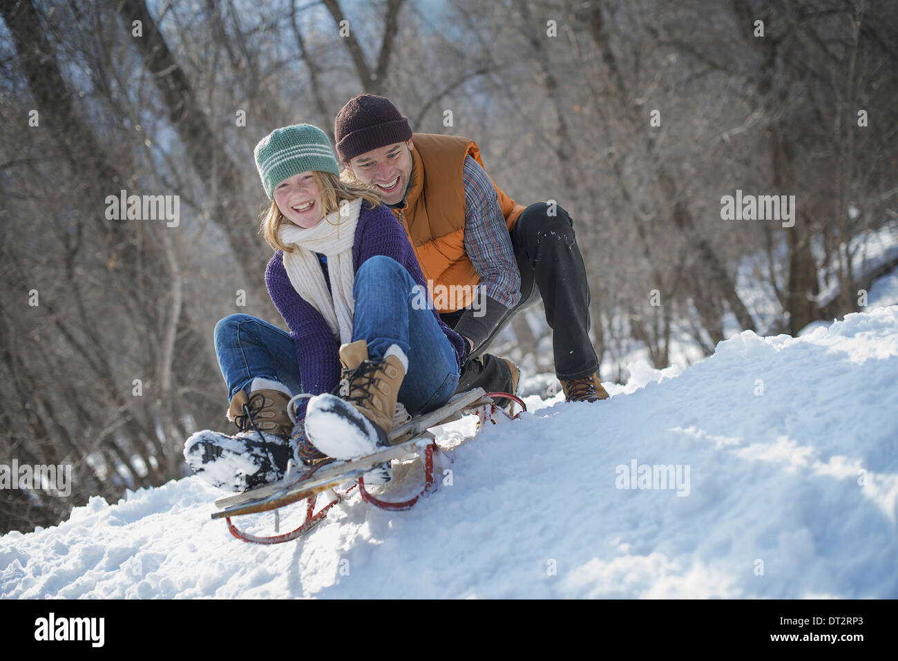 Paysage d'hiver avec neige au sol un homme poussant une jeune femme du haut d'une pente sur un toboggan Banque D'Images