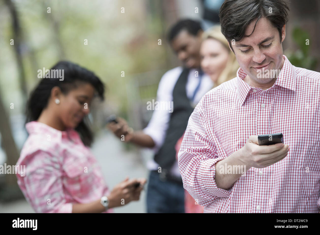 Vue sur cityYoung les gens à l'extérieur dans un parc de la ville trois personnes contrôler en regardant leur téléphone cellulaire Banque D'Images