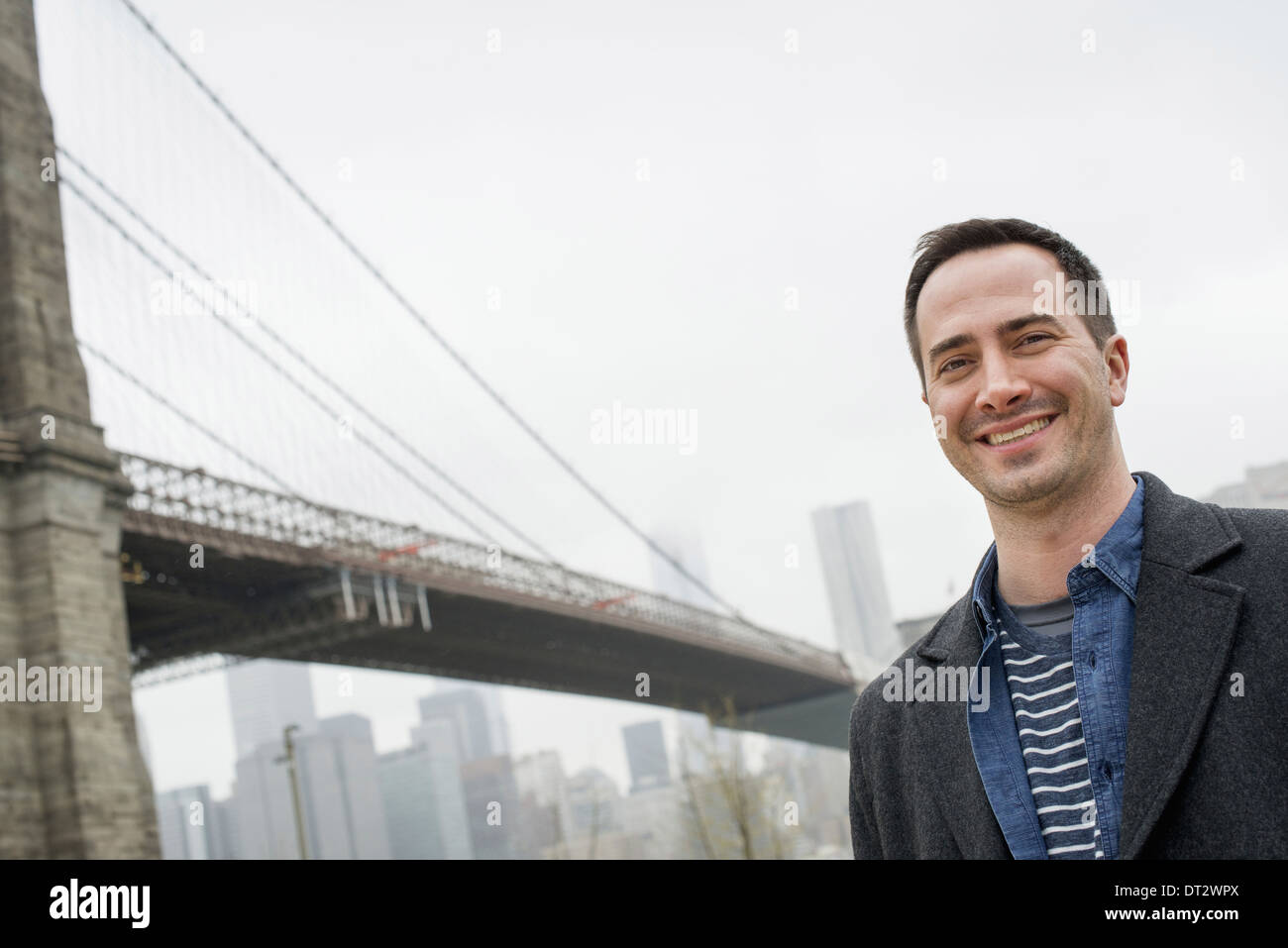 New York le pont de Brooklyn, traversée de la rivière de l'est un homme portant un manteau gris smiling at the camera Banque D'Images