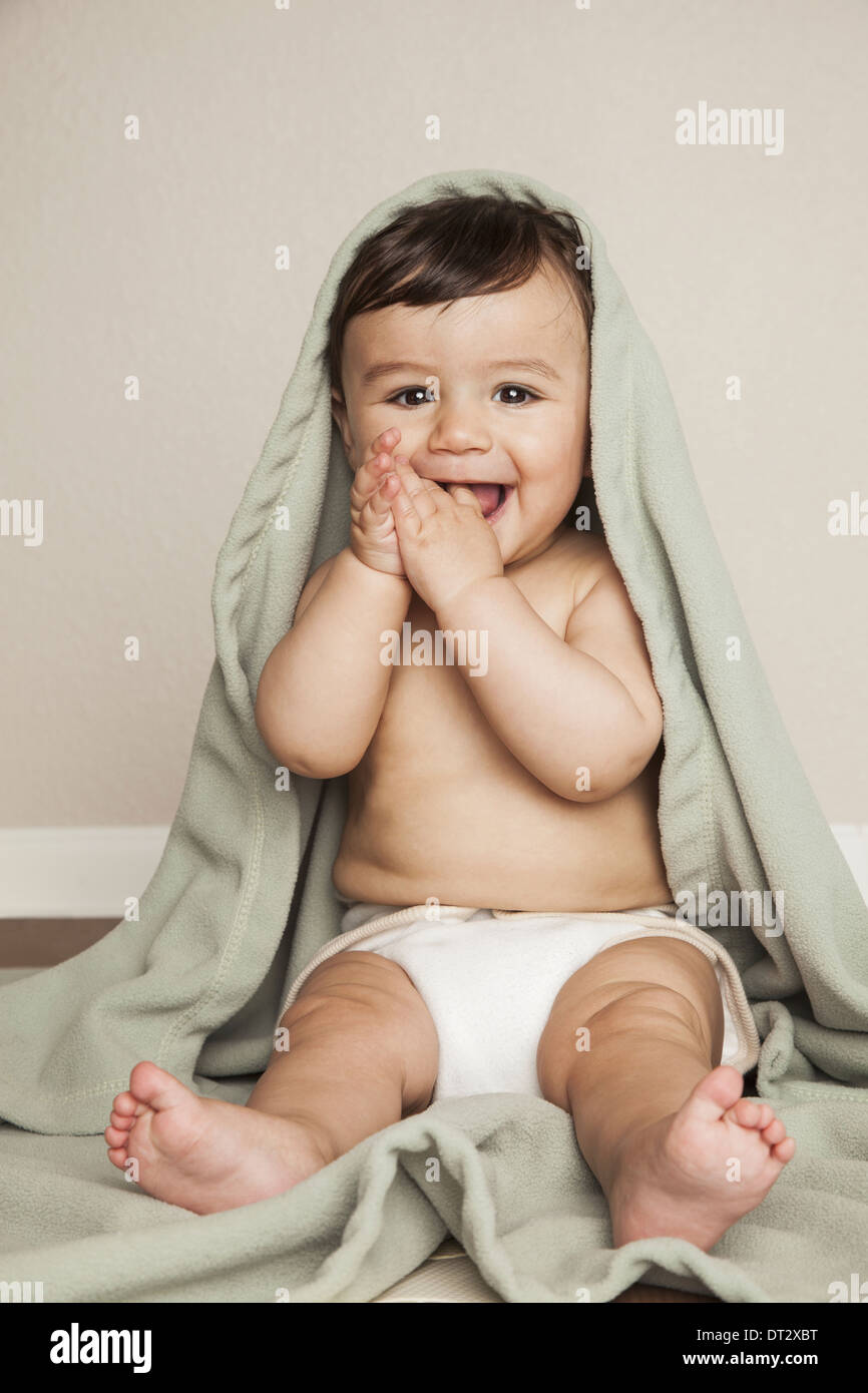 Un jeune garçon bébé 8 mois portant des couches en tissu assise sur le sol une couverture sur la tête de bébé Banque D'Images
