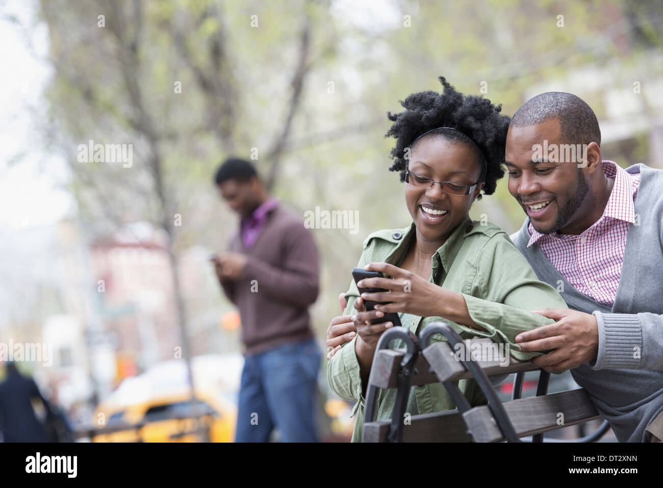 Une femme et un homme sur un banc, contrôler son téléphone deux hommes dans l'arrière-plan Banque D'Images