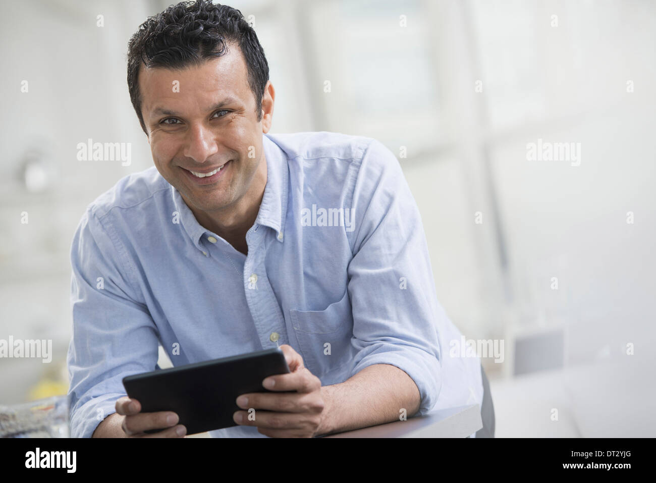 Un homme en chemise bleue s'appuyant sur un bureau d'une holding digital tablet Banque D'Images