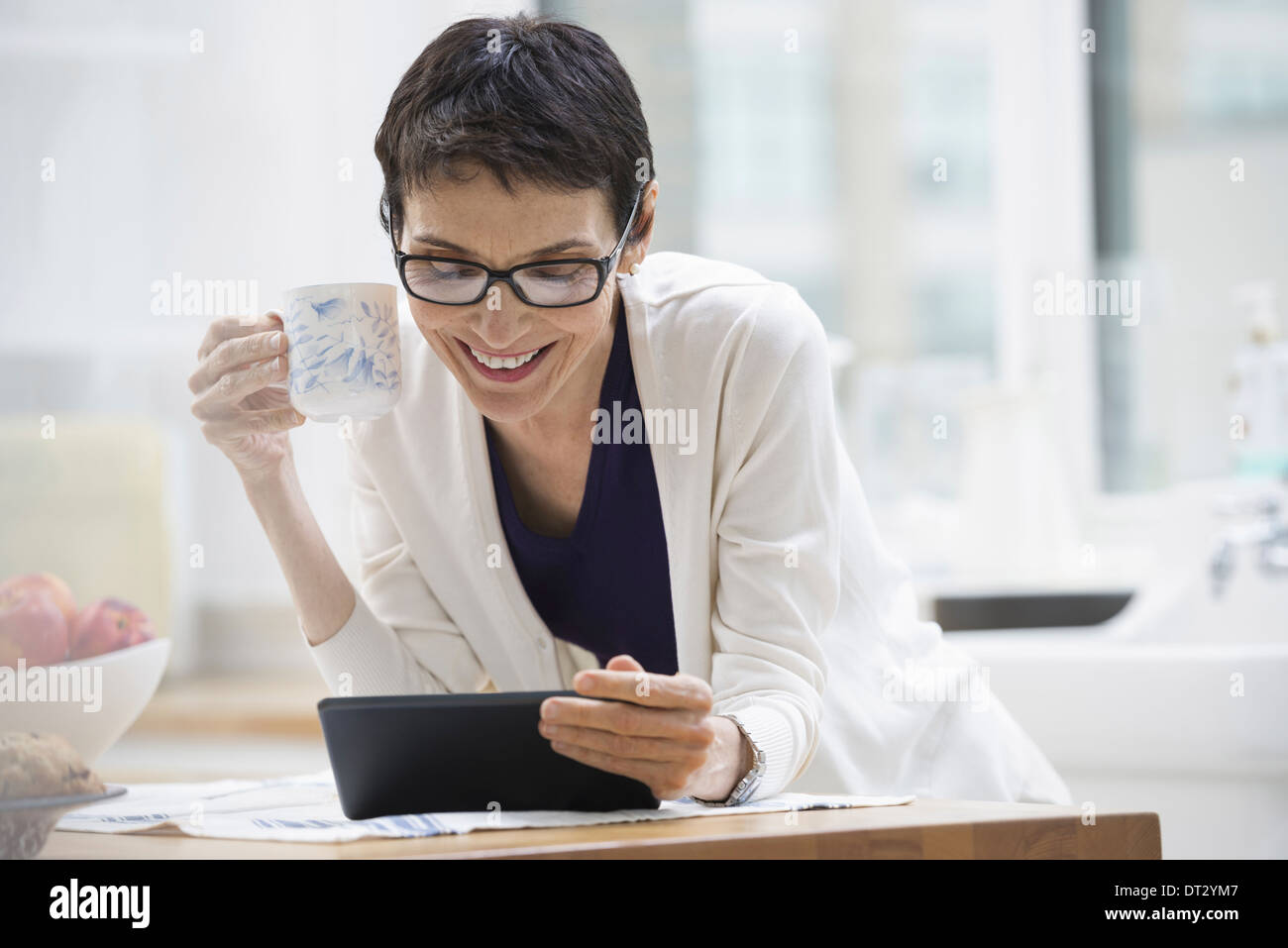 La ville de New York une femme habillée pour travailler en veste crème tenant une tasse de café contrôler sa tablette numérique Banque D'Images