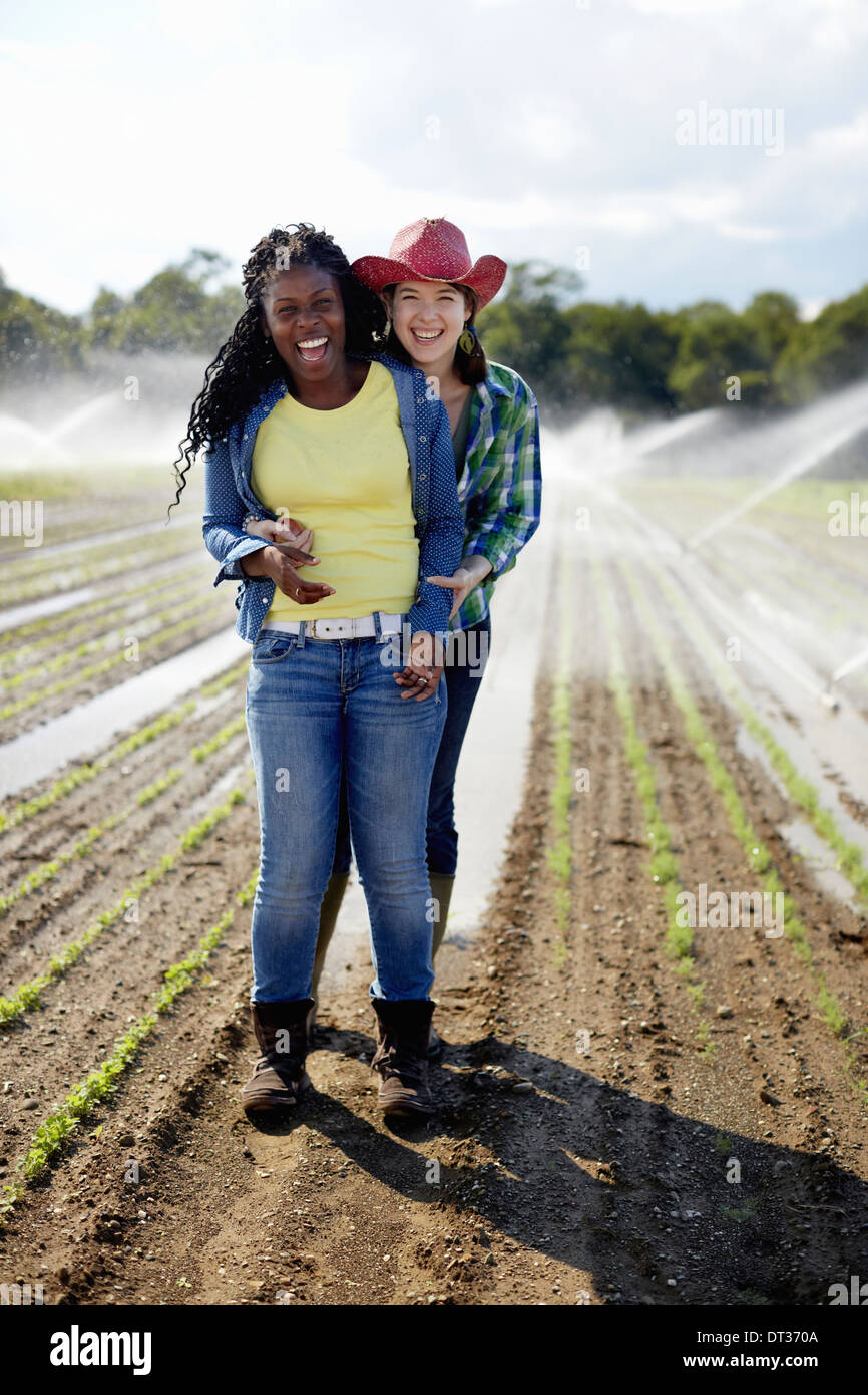 Deux jeunes femmes debout dans un champ de petites plantules avec les têtes d'irrigation arrosant le sol Banque D'Images