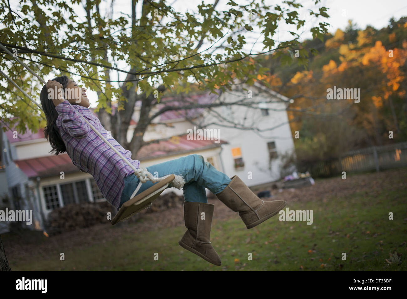 Une ferme, jardin éclairé par les arbres d'automne la fin de l'ensoleillement. Un enfant assis sur une balançoire. Banque D'Images