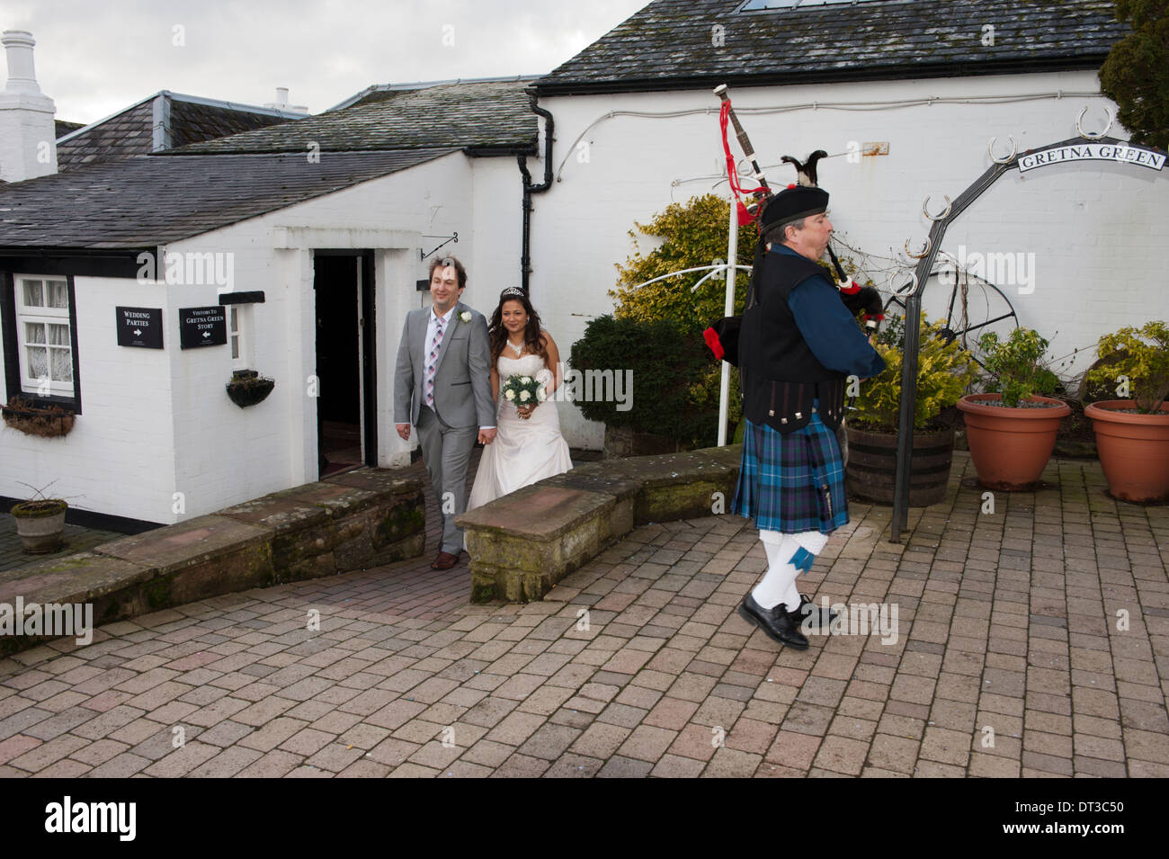 Un couple nouvellement marié à pied de la vieille forge à Gretna Green, l'Écosse, précédé d'un Piper Banque D'Images