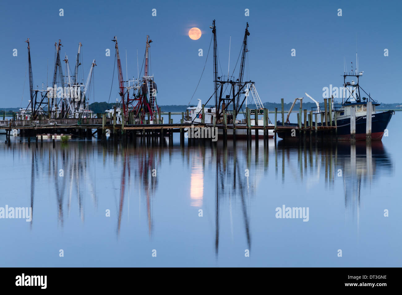 Bateaux de crevettes à un quai avec la pleine lune dans l'arrière-plan. Banque D'Images