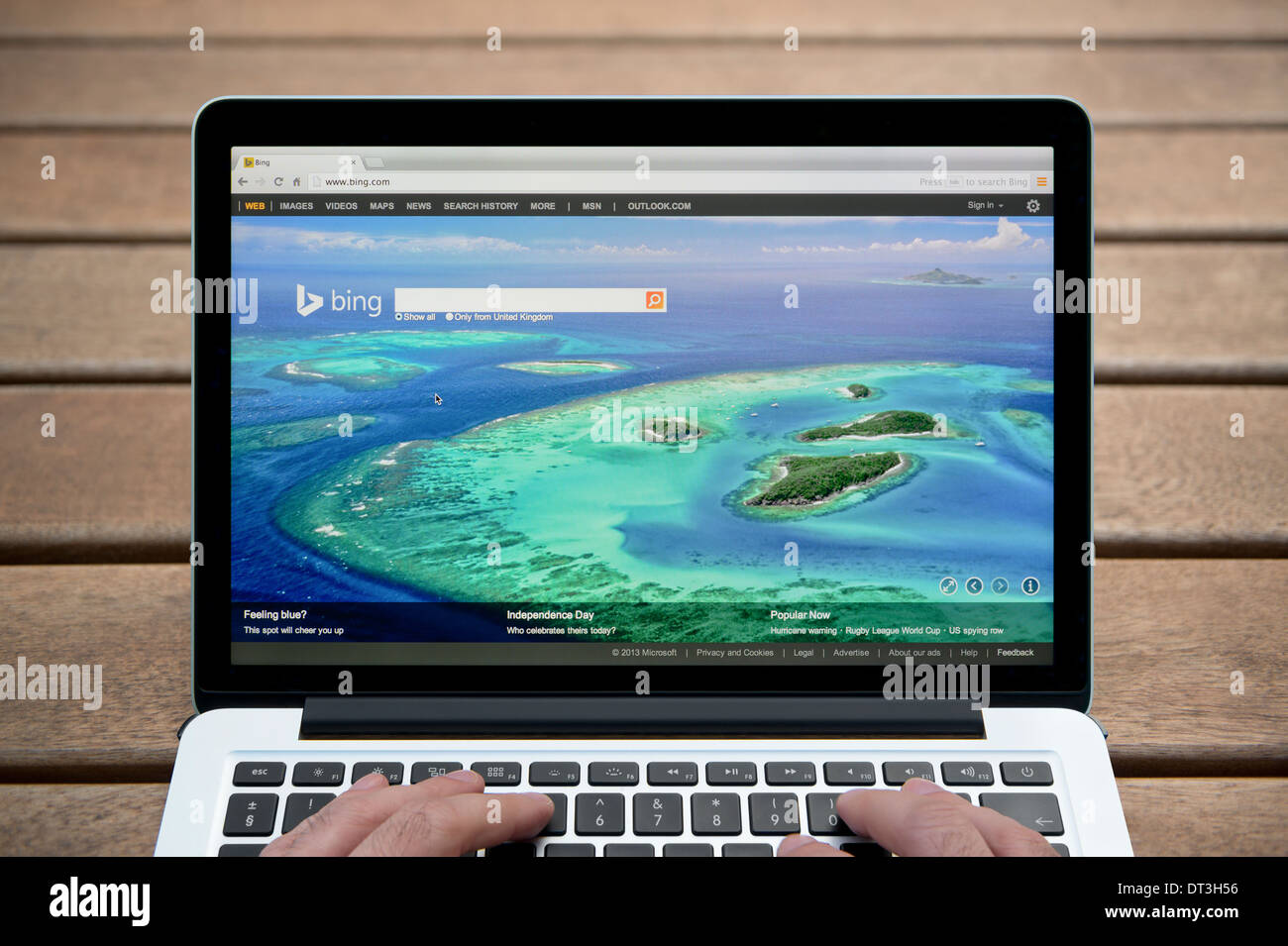 Le site web de Bing sur un MacBook contre un banc en bois fond de plein air y compris les doigts d'un homme (usage éditorial uniquement). Banque D'Images