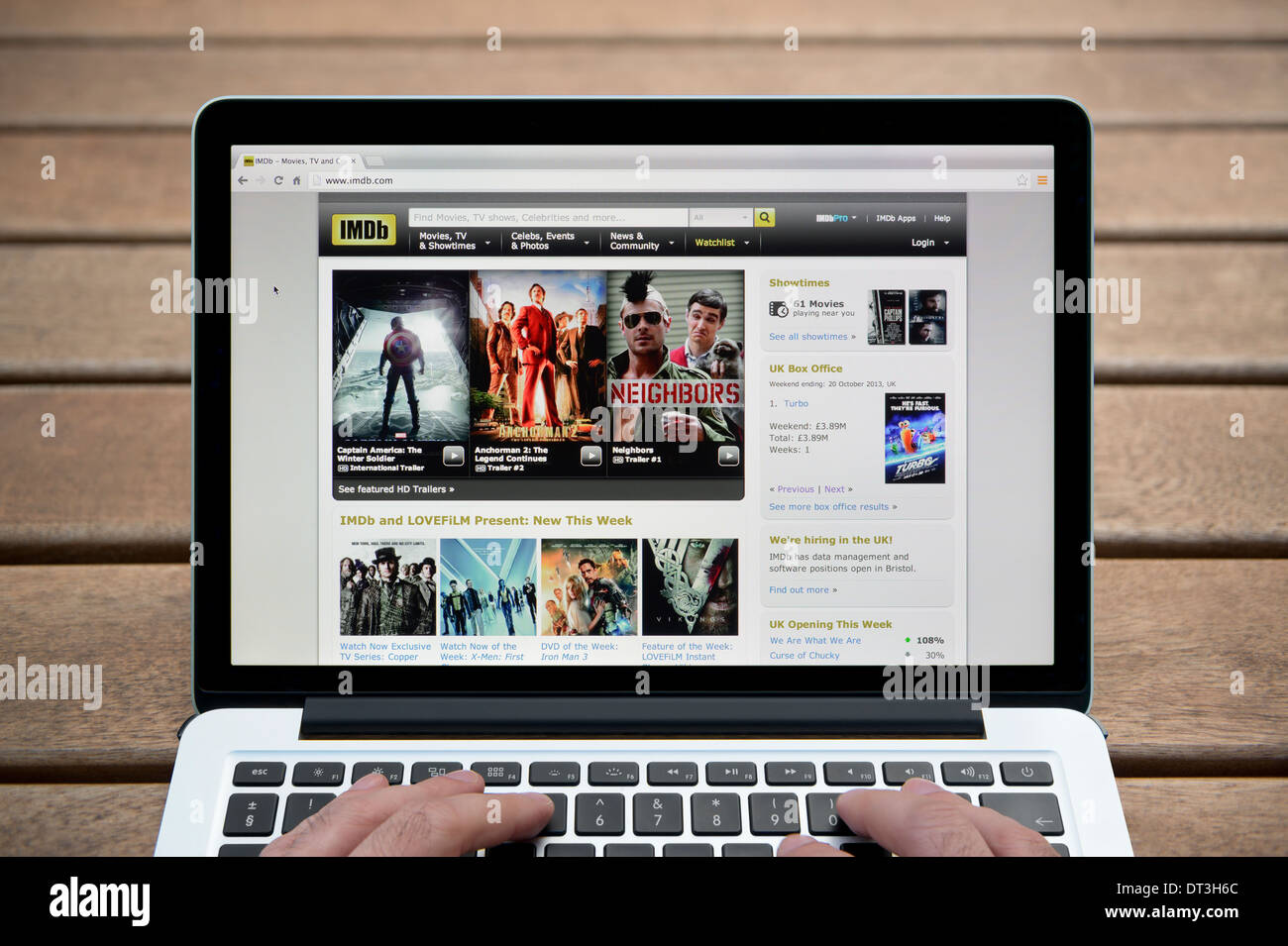 L'IMDb site sur un MacBook contre un banc en bois fond de plein air y compris les doigts d'un homme (usage éditorial uniquement). Banque D'Images
