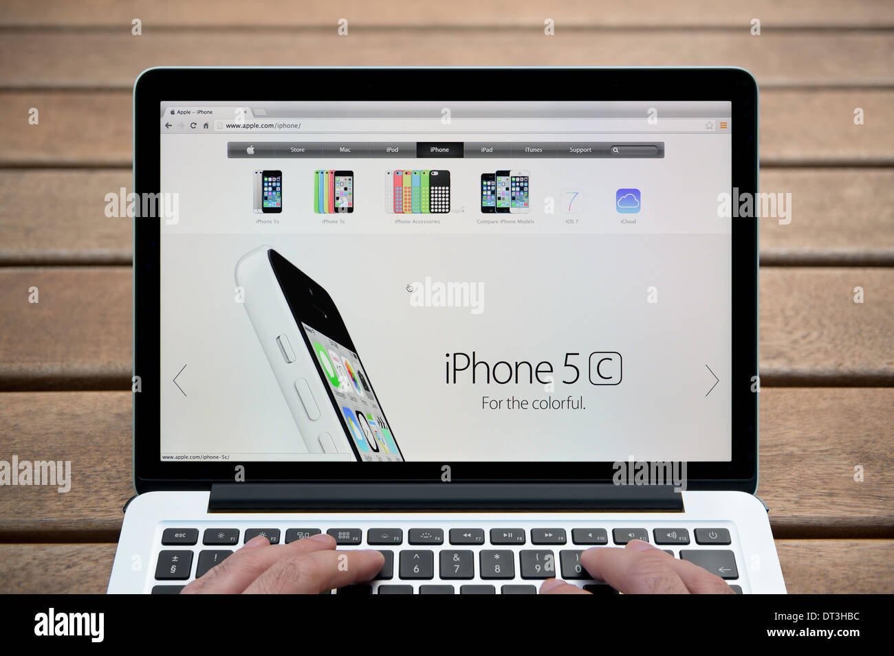 Le site web de l'iPhone d'Apple sur un MacBook contre un banc en bois fond de plein air y compris les doigts d'un homme (usage éditorial uniquement). Banque D'Images