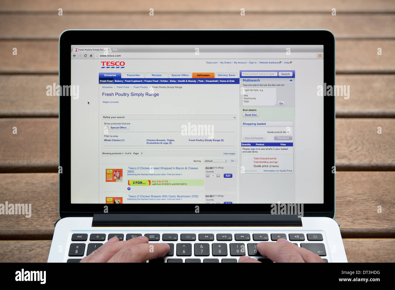 Le site web de Tesco sur un MacBook contre un banc en bois fond de plein air y compris les doigts d'un homme (usage éditorial uniquement). Banque D'Images