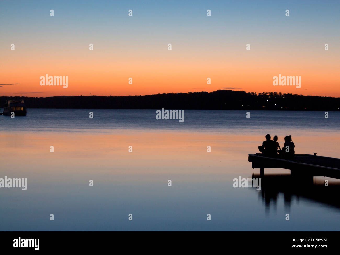 La silhouette de la famille assis sur fin de Warners Bay jetty at sunset Lake Macquarie NSW Australie Nouvelle Galles du Sud Banque D'Images