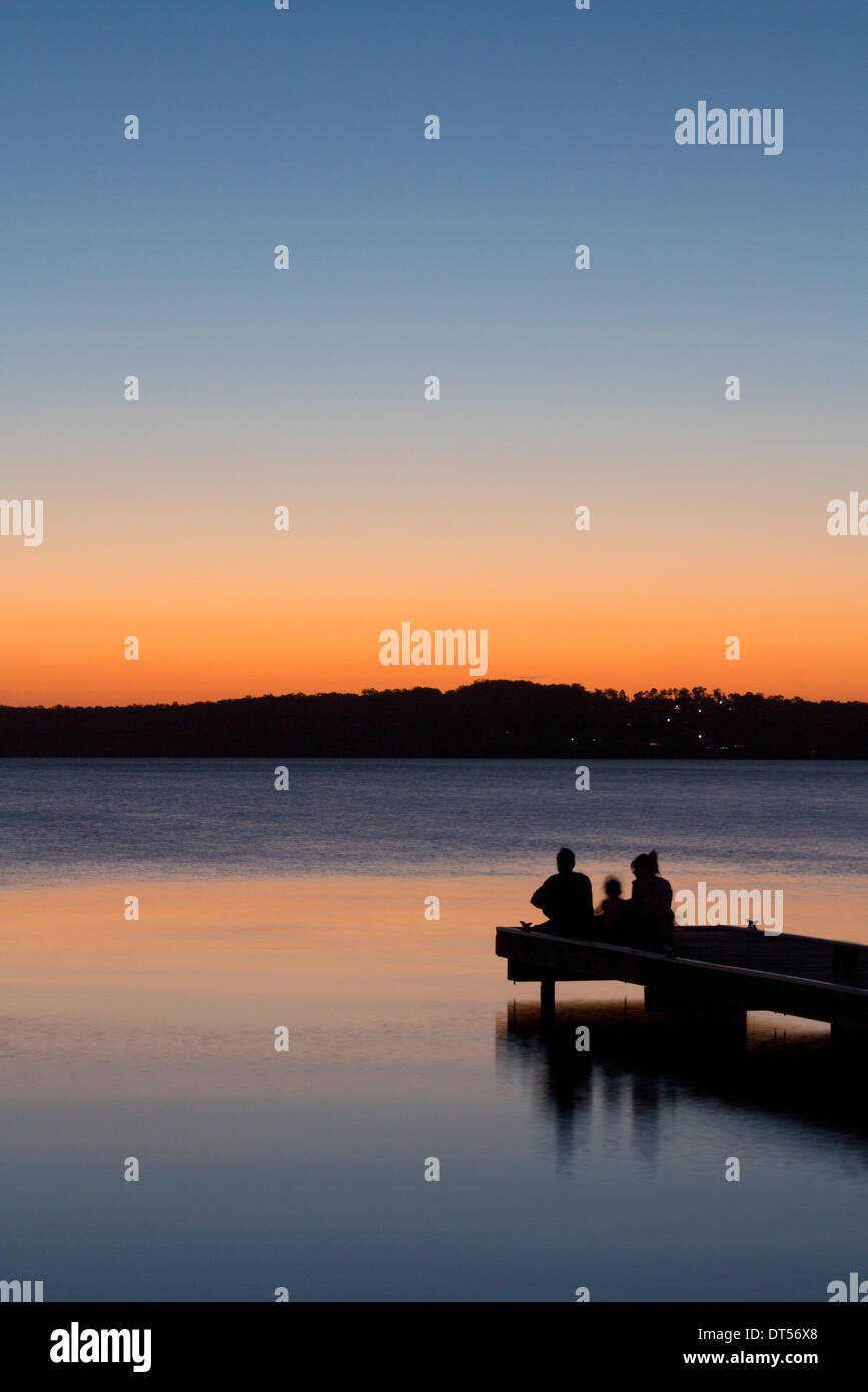 La silhouette de la famille assis sur fin de Warners Bay jetty at sunset Lake Macquarie NSW Australie Nouvelle Galles du Sud Banque D'Images