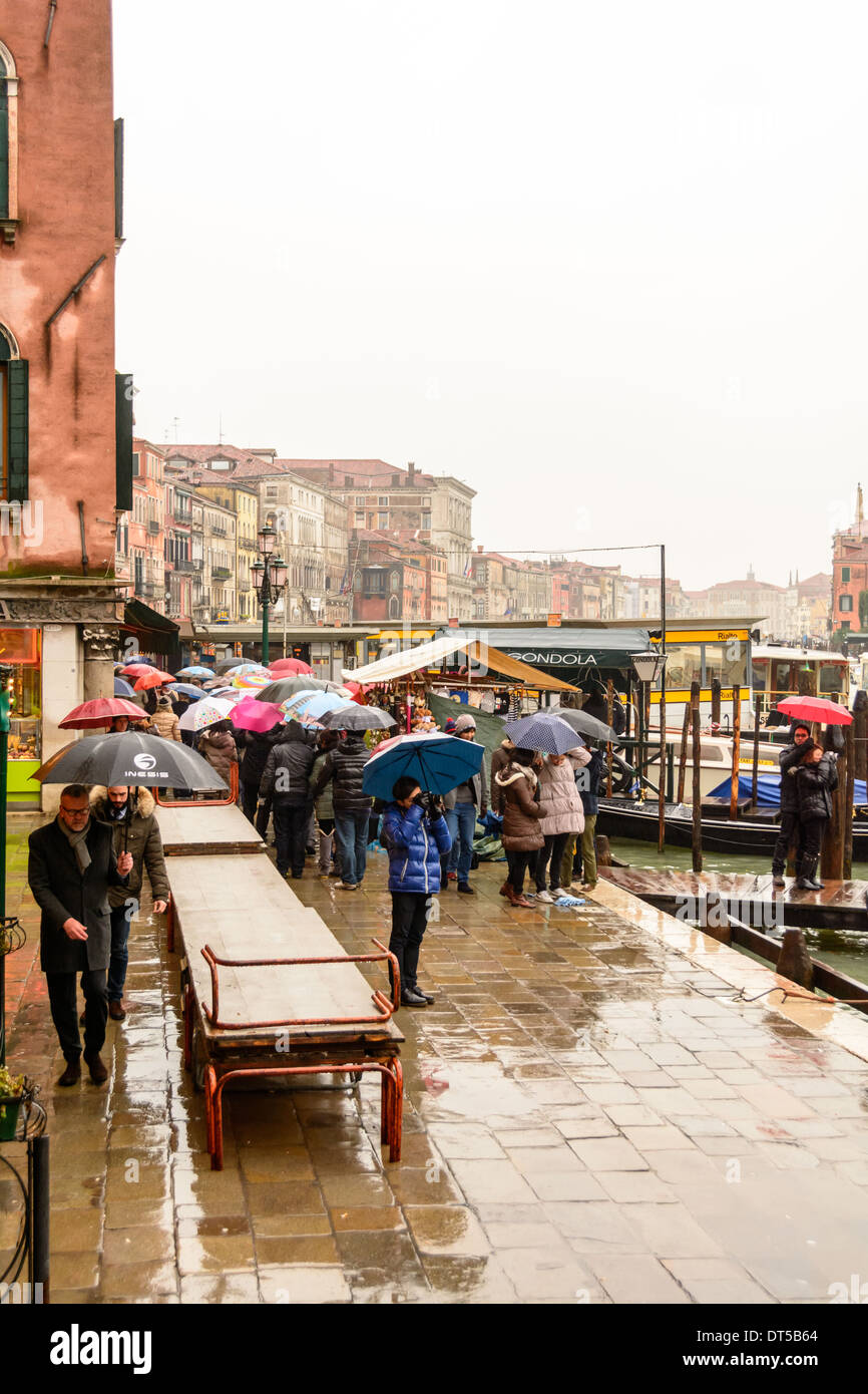 Venise, Italie sur une journée pluvieuse, la préparation de acqua alta (haute) de l'eau avec les passerelles sur le trottoir et les gens en attente à l'arrêt de vaporetto Rialto (gare). Banque D'Images