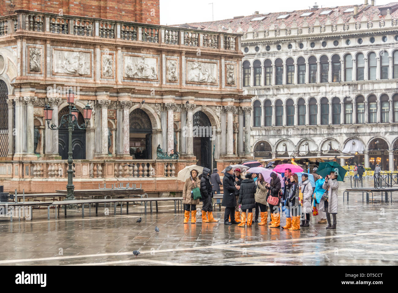 Venise, Italie. Les touristes asiatiques par temps humide, parapluies, vêtements et bottes de pluie orange sur la Place St Marc, Le Campanile de l'entrée. Banque D'Images