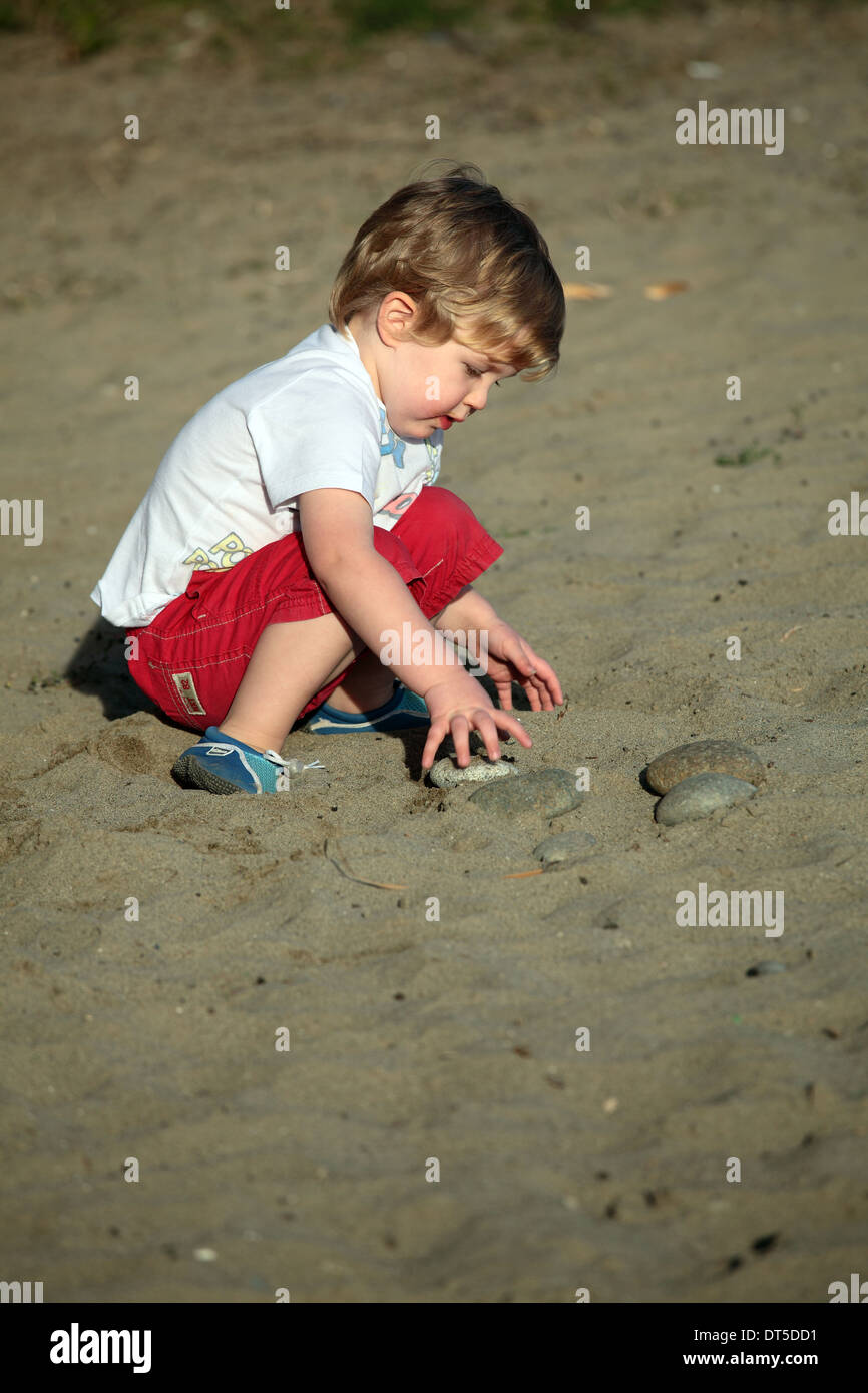 Petit Garçon jouant avec des pierres sur une plage Banque D'Images