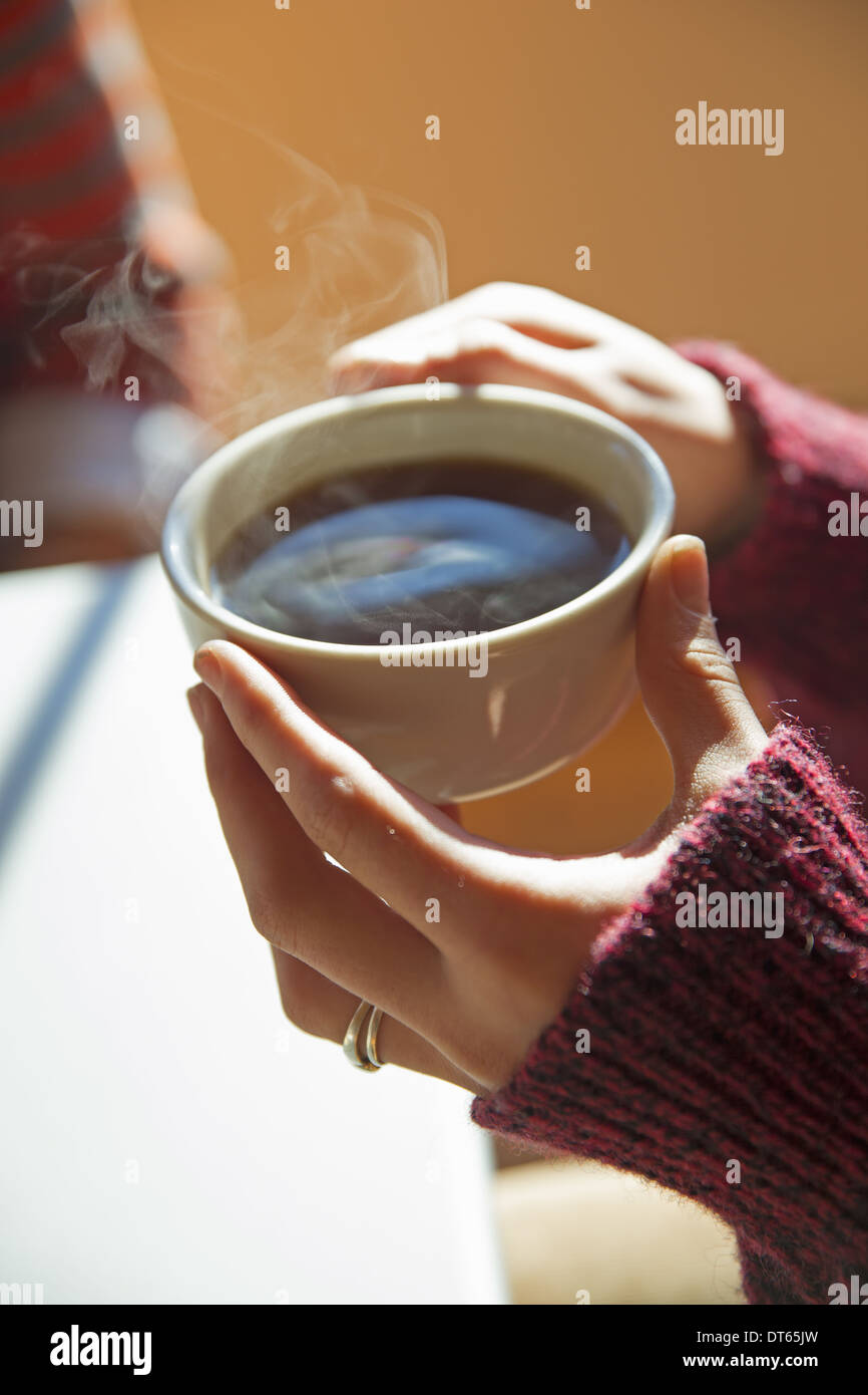 Une femme tenant une tasse de café chaud dans ses mains. Banque D'Images