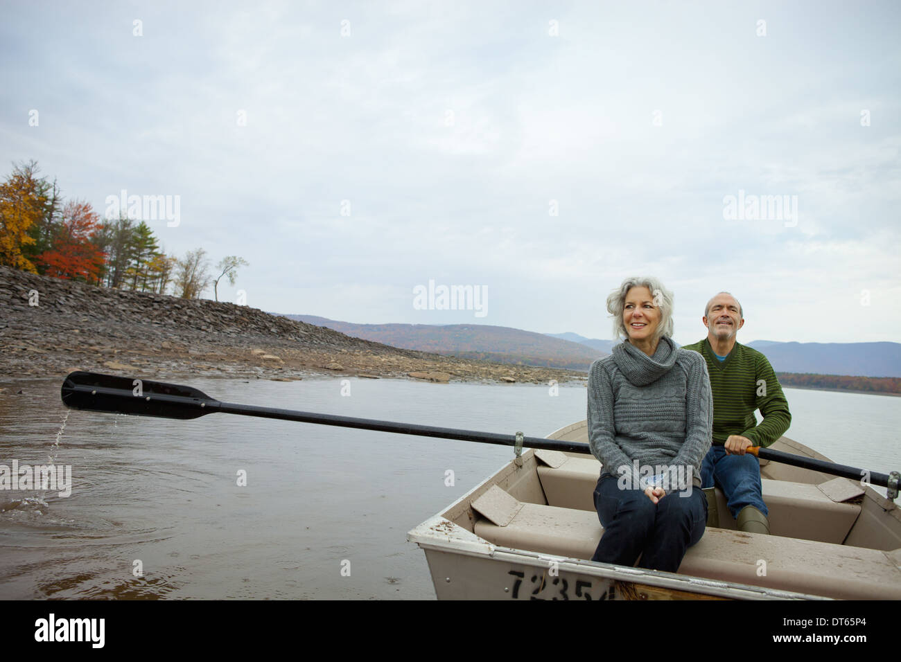 Un couple, homme et femme assis dans un bateau à rames sur l'eau une journée d'automne. Banque D'Images