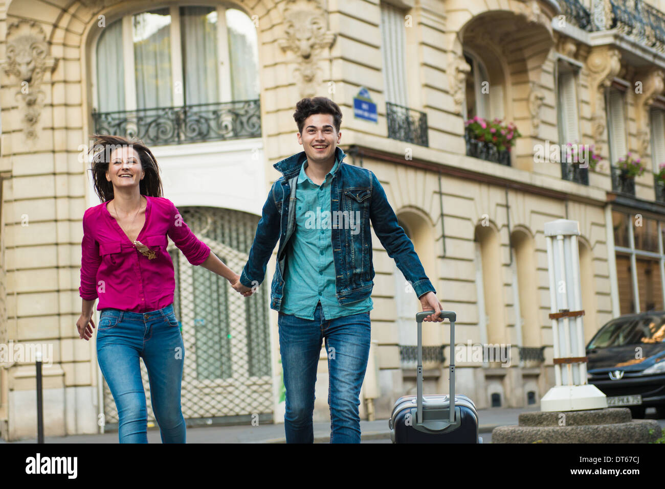 Jeune couple en train de marcher avec valise à roulettes, Paris, France Banque D'Images