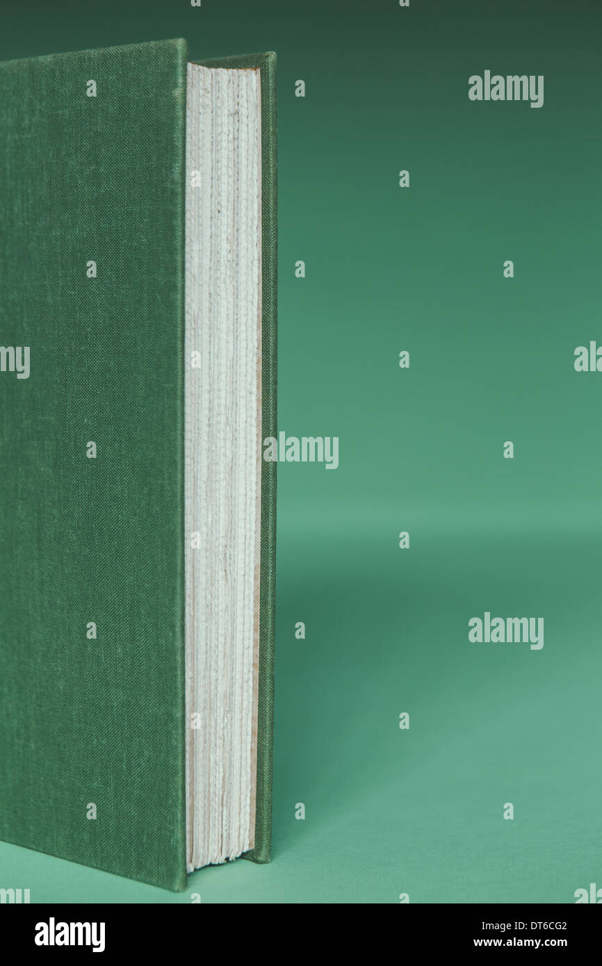 Un livre avec une couverture verte, papier blanc et bords de page, debout sur un fond vert. Banque D'Images