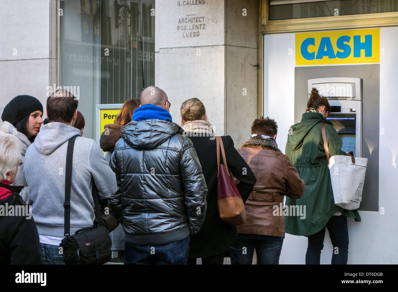 Les clients en attente dans la file d'attente pour recueillir de l'argent au distributeur Le distributeur de billets de banque dans la rue commerçante en hiver Banque D'Images