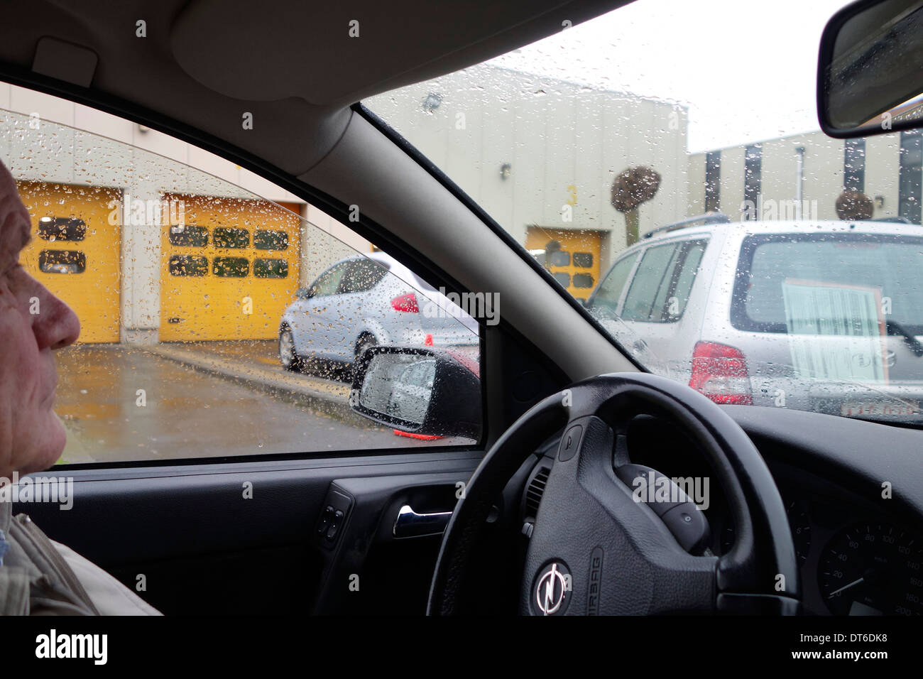 Homme âgé en attente dans la file de voiture en face de la porte du centre d'essai pour un mot d'inspection annuelle Banque D'Images