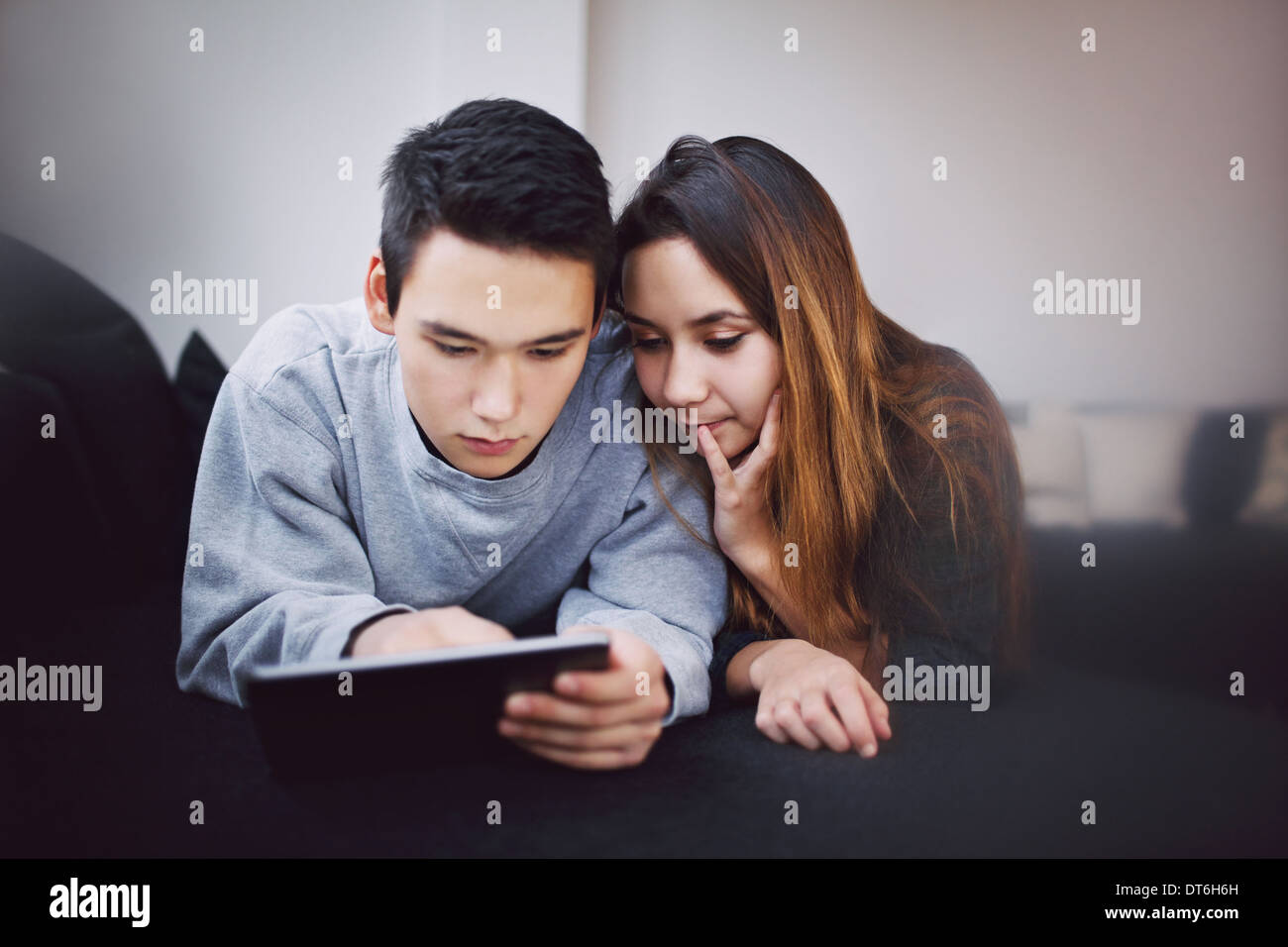 Teenage couple surfing sur Internet tablette numérique en position allongée sur un canapé à la maison. Mixed Race woman using tablet couple sur la table. Banque D'Images