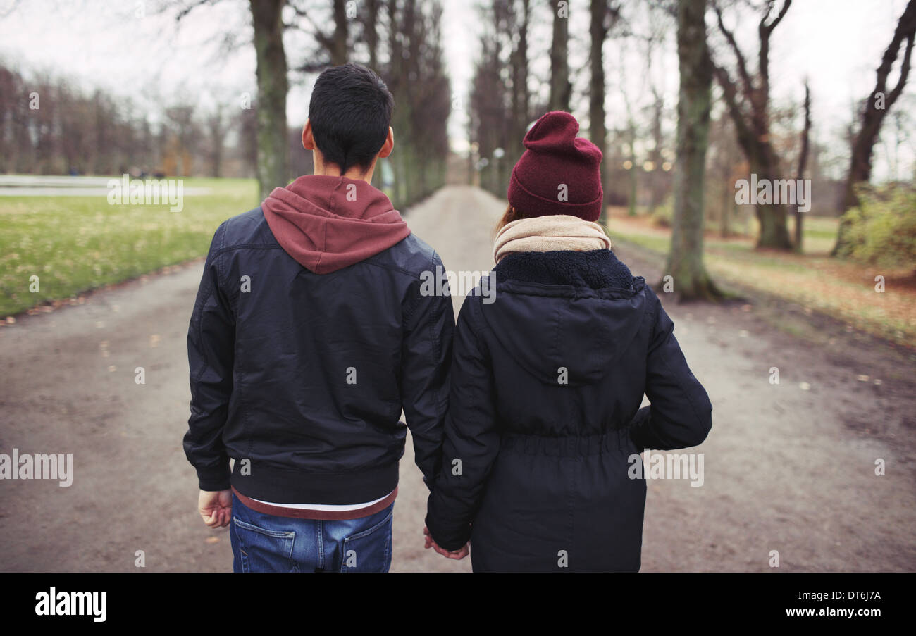 Vue arrière du couple walking in park se tenant la main. Jeune homme et femme dans des vêtements chauds à l'extérieur. Banque D'Images