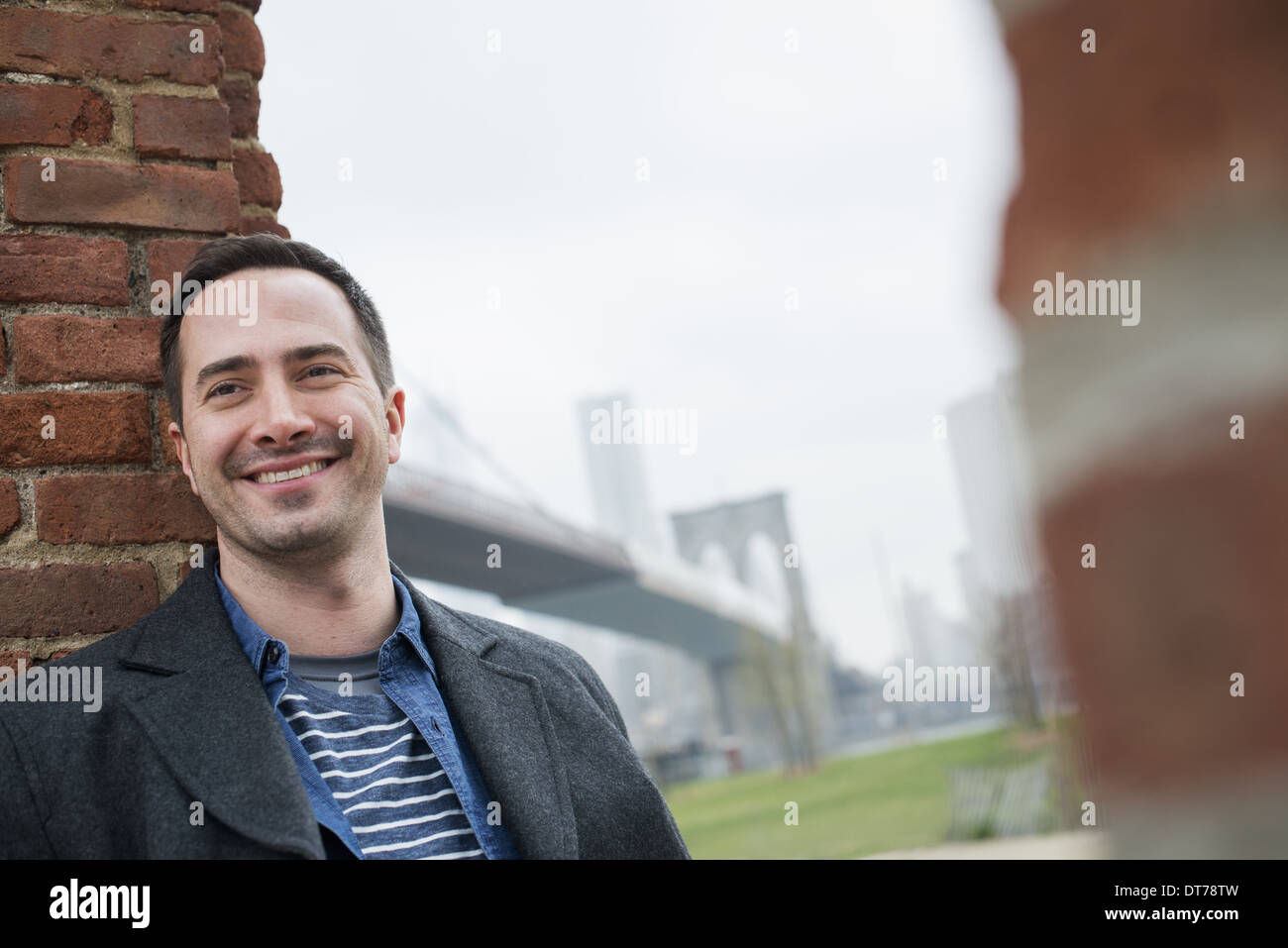 La ville de New York. Le Pont de Brooklyn, traversée de l'East River. Un homme appuyé contre un mur de briques. Banque D'Images
