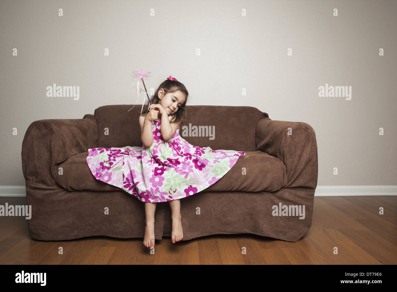 Une fillette de 3 ans avec de longs cheveux bruns dans une robe de coton fleuri rose avec la jupe distribués, en agitant une baguette. Banque D'Images