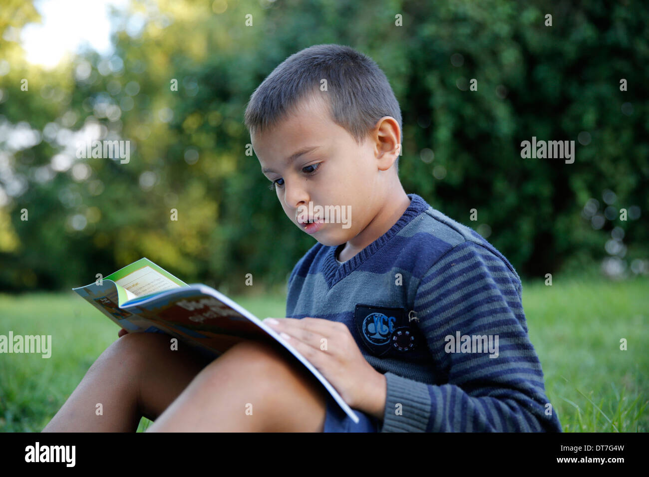 Garçon de 7 ans la lecture d'un livre chrétien dans un jardin Banque D'Images
