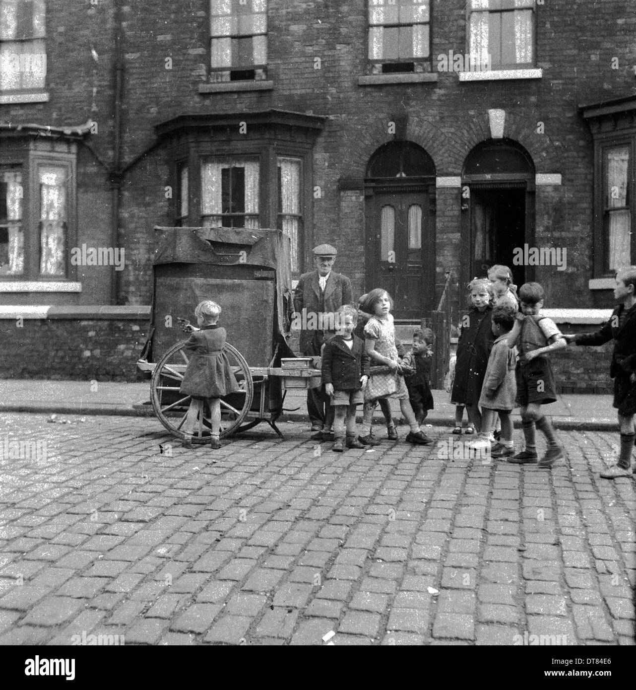 Image historique des années 1950 montrant un groupe d'enfants du centre-ville dans une rue pavée avec un vieil homme en forme de tissu osseux debout près de son chariot. L'homme était un commerçant recueillerait les articles ménagers non désirés et jetés - vieux vêtements, bicyclettes, articles en métal, morceaux de meubles etc - et les revenait ensuite. Un recycleur d'un seul homme. Banque D'Images